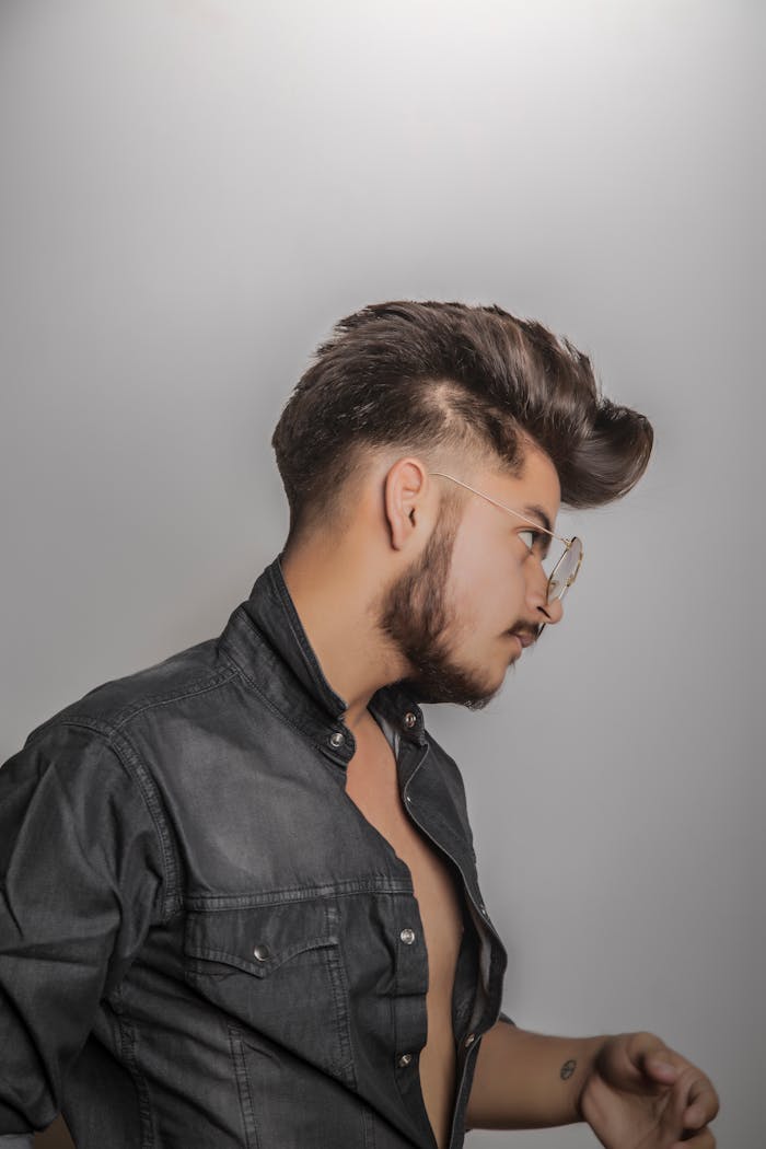 Side view of a stylish man with glasses and denim shirt, showcasing trendy hairstyle.