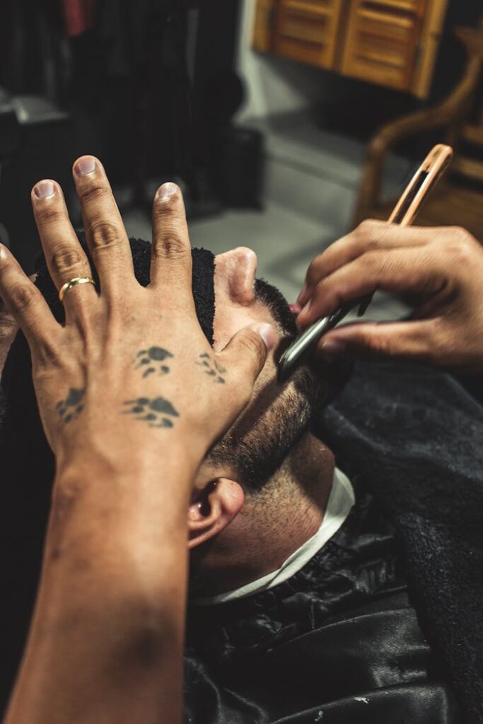 The Art of Drawing Readers In: Your attractive post title goes here A barber using a straight razor to shave a man's face indoors, showcasing tattooed hands.
