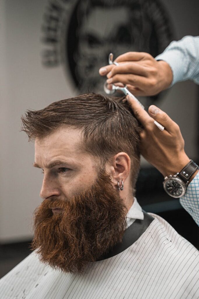 Crafting Captivating Headlines: Your awesome post title goes here Close-up of a barber styling a bearded man's hair indoors. Side view capturing the precise haircut process.